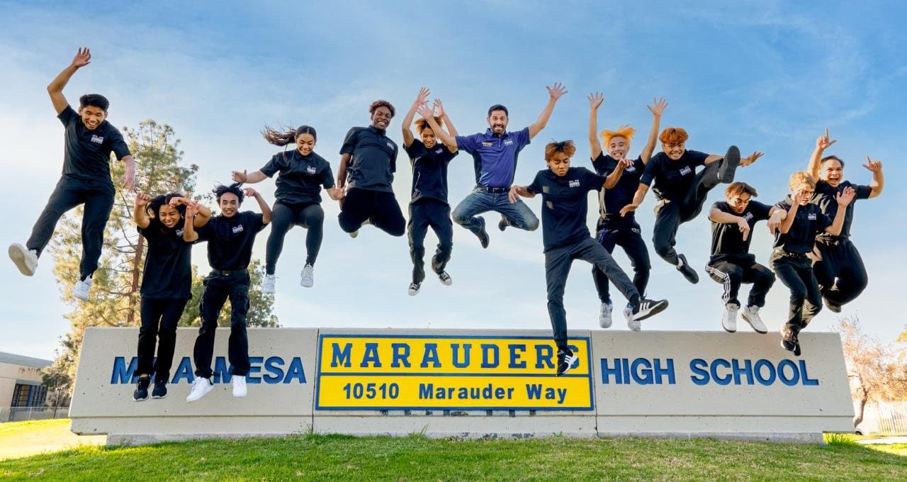 Mira Mesa wrestlers leaping in joy in front of the Mira Mesa High School Marauders sign